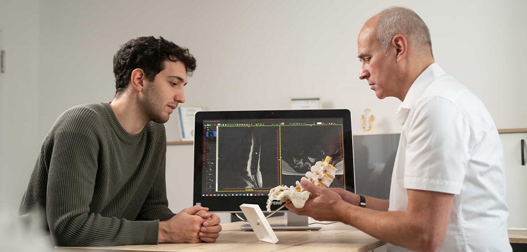 Dr. Wiedenhöfer erläutert Patienten Befund an Modell der Halswirbelsäule