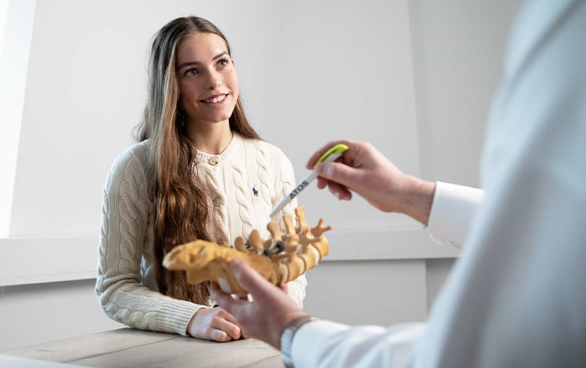 Arzt erläutert Patientin Befund am Modell der Lendenwirbelsäule